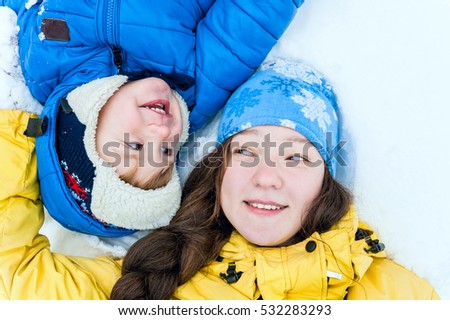 Outdoor portrait Happy sister and brother lying on the snow in winter park and smiling