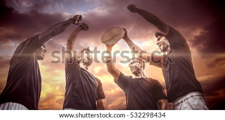 3D Blue and orange sky with clouds against rugby players cheering together with ball