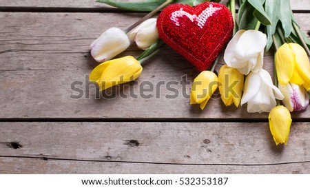 Yellow and white spring tulips and shiny decorative heart on aged wooden background. Selective focus. Place for text.