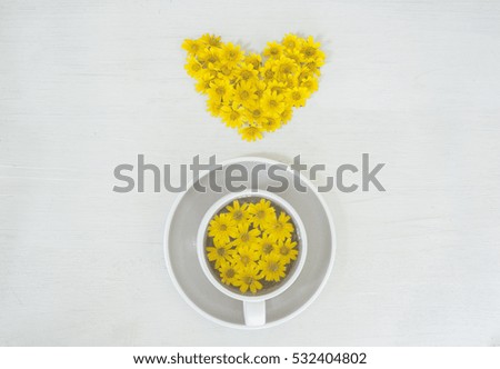 still life with tea cup and yellow flowers shape of heart on white background.

