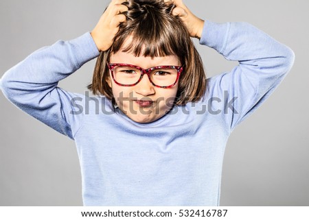 annoyed 6-year old little child with eyeglasses scratching her head for small tantrum or pulling out her hair for itchy lice or allergies, grey background 