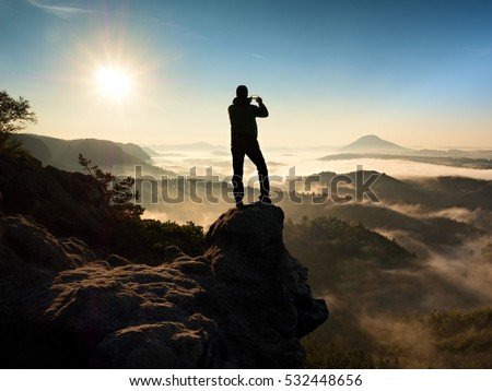 Tourist takes photos with smart phone on peak of hilly landscape. Autumn fogy hills, man photograph misty sunrise in hills and mountains.