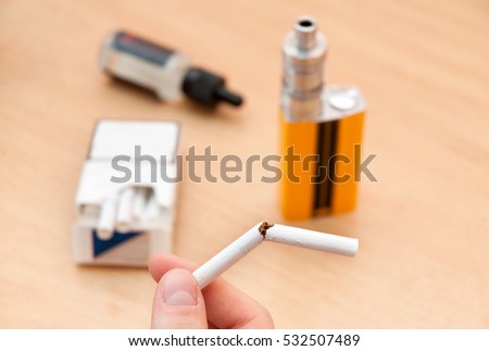 Human fingers holding a broken cigarette in the background of the e-cigarette
