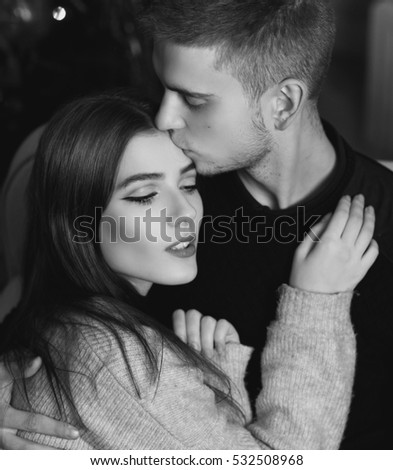 Closeup portrait of young romantic caucasian couple sitting and hugging in christmas decorated interior. Cute lovers staying at home and enjoying tome together