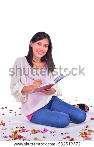 Beautiful woman sitting on the white floor while writing a letter surrounded by rose petals