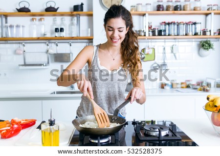 Portrait of young woman frying onion into the pan in the kitchen. Royalty-Free Stock Photo #532528375