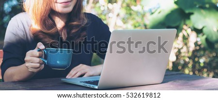 A beautiful asian woman using laptop with feeling happy and smiley face , sitting  in green nature outdoor background 