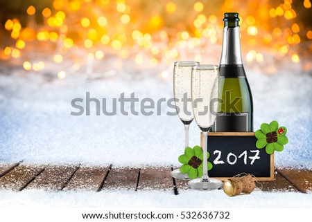 new years eve champagne bottle glasses and empty slate blackboard chalkboard wooden frame decorated with  four leaf clover and ladybug snow bokeh background