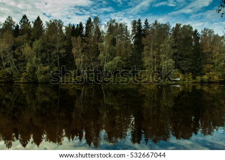 Trees and blue sky are reflected in calm water