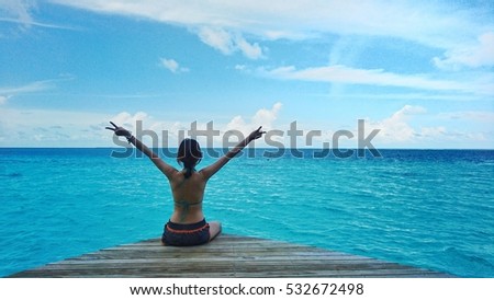 Model sitting at terrace with hans up in the air, Maldives