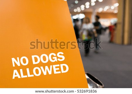 Word "NO DOGS ALLOWED" on orange banner board and trashcan with blur image of people in exhibition or shopping mall.