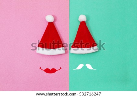 Two red Santa Claus hats on pink and  blue-green color paper background with male and female hipster faces. Pop Art Design, Minimal Creative pop-art style
