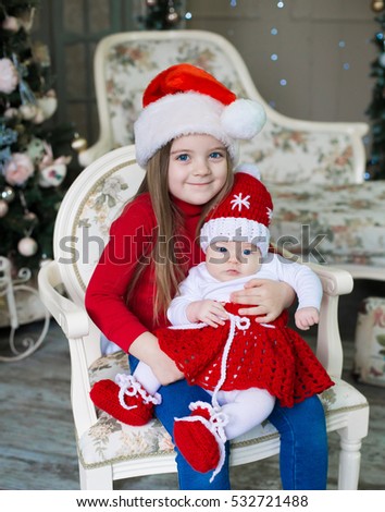 Beautiful little blonde baby girls, has happy fun cheerful smiling face, blue eyes, has red Christmas hat Santa Claus. Portrait holiday. Close up. Winter background. Family portrait