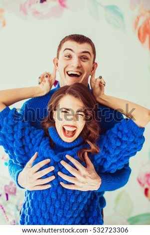 Funny man in blue sweater puts his arms on lady's breast while she tries to catch his ears