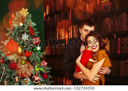 Beautiful young couple holds little chihuahua in red sweater standing before Christmas tree