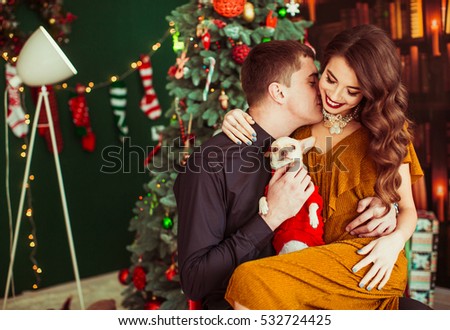Man kisses neck of stunning woman sitting with her before Christmas tree