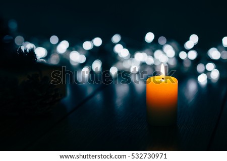 Burning candle on a table with Christmas decorations pine cones and a box on the background of garlands,