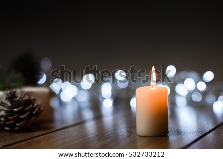 Burning candle on a table with Christmas decorations pine cones and a box on the background of garlands,