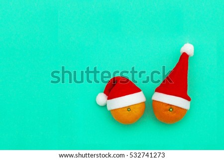 Christmas backgraund, copy space, text place. Two Orange Clementine in red Santa Claus hats on blue-green color paper background.  Merry Christmas and New Year Happy Holidays