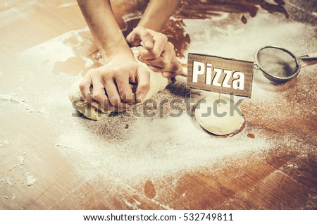 woman hand pressing dough on the table. Paper with pizza text ahead dough