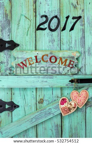 Year 2017 sign in black iron numbers, WELCOME and peach country fabric floral hearts on antique rustic mint green wood door; painted wooden copy space for text