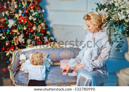 Cute little baby boy and his mother. Vintage style. Christmas background with gifts and Christmas tree.Mom playing with his son on a retro couch