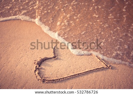 Heart drawn on the beach sand being washed away by a wave. Toasted sand tone. Love affair, summer love or breakup and divorce concept. Ephemeral romantic love. Not true love. End of relationship. Royalty-Free Stock Photo #532786726