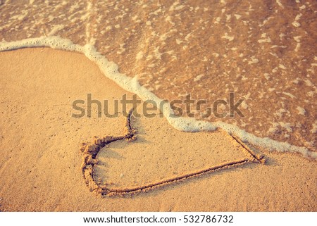 Heart drawn on the beach sand being washed away by a wave. Sand tone. Love affair, summer love or breakup and divorce concept. Ephemeral romantic love. Not true love. End of relationship. Royalty-Free Stock Photo #532786732