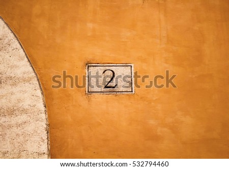 Engraved building number (2) on orange colour, old wall in Rome.