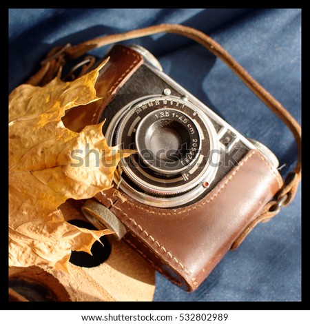 Still life of a vintage 35mm film camera in a leather case, with autumn leaf, on a dark blue background