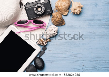 Straw hat sunglasses and photocamera among sea shells and stones on wooden surface