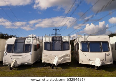 Three Caravans stored in rows on a sunny day with clouds in the sky with electricity cables in the background. Space for text. Royalty-Free Stock Photo #532846867