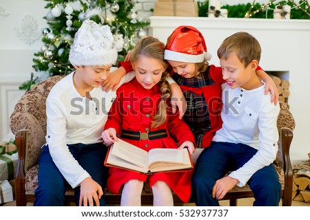 Kids reading a story book together under a Christmas tree on Christmas time at home