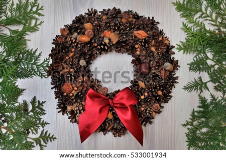 decorative wreath with cones and red bow on wooden background