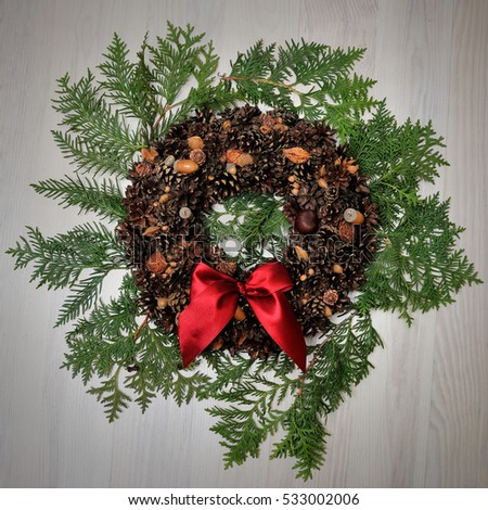 decorative wreath with cones, red bow on coniferous branch andwooden background