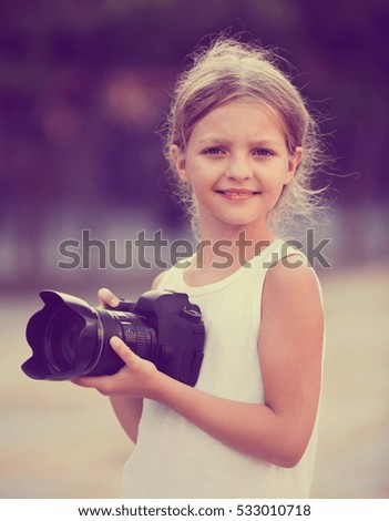 Glad  girl taking pictures with professional camera outdoors on summer day