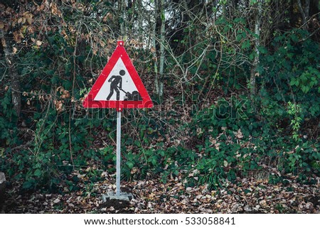 Under construction sign with a digging worker with a shovel on a red sign in a green forest