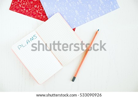 Flat lay of blank notepad for make plans, pencil, decorated Christmas papers. White table. Fashion blogger goals. New year resolution planning