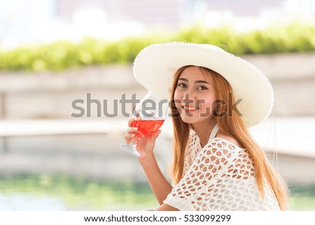 Beautiful woman with white hat holding fresh juice near pool