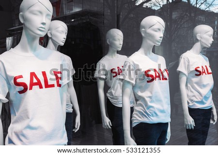 Window display with five mannequins wearing t-shirts with text Sale