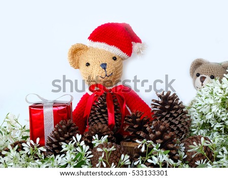 Cute crochet teddy bear Santa claus doll with pine cone on white Christmas flower background 