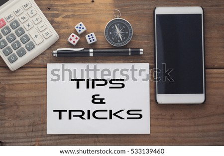 Tips & Tricks written on paper,Wooden background desk with calculator,dice,compass,smart phone and pen.Top view conceptual.