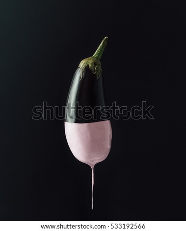 Eggplant with dripping pink paint on dark background. Minimal food concept.