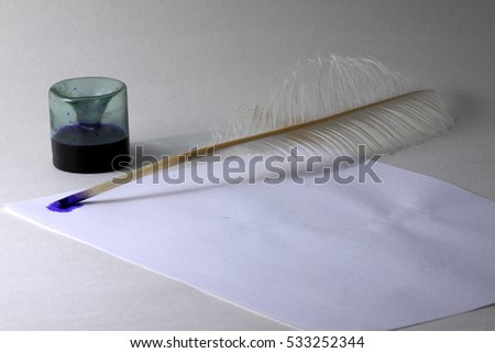 Ink-pot with a feather of a goose on a white background and a blank sheet of paper
