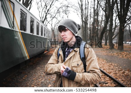 A young guy in a jacket with a backpack near train.