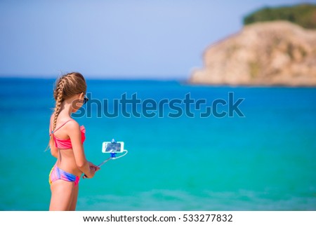 Little girl taking selfportrait by cellphone on the beach. Kid enjoying her suumer vacation and making photos background the sea