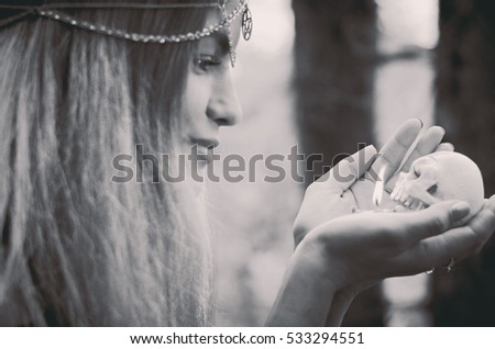 Young witch with a skull candle in her hands, black and white photo, soft focus, faded colors 