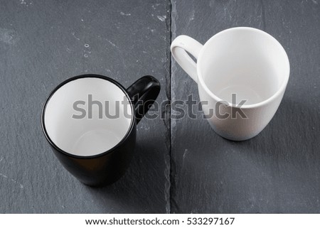 This is a simple picture of two cups on a grey, slate, background. Slate background. Slate table. White/ Black cup. Both cups are empty. Space for text.