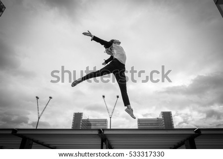 Beautiful young woman in a strict black and white jacket doing contemporary jazz dance moves jumping over two skyscrapers of a modern business district
