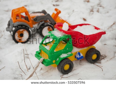 Children's winter games outdoors with toy excavator and toy cars. The image of a child making playing with a large colourful toy car.